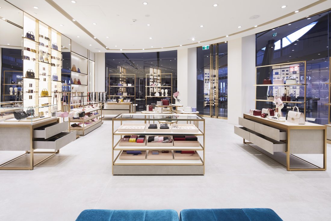 Luxury accessories boutique interior with illuminated display walls, sleek counters and handbags arranged on elegant shelving.