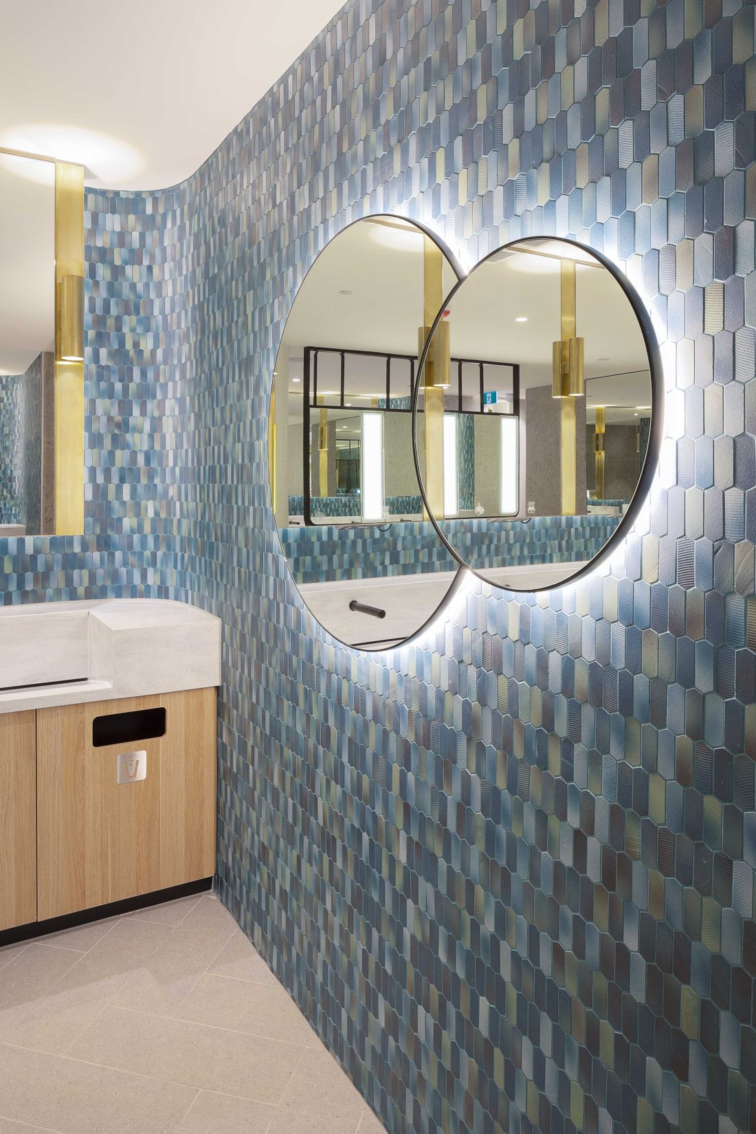 Contemporary bathroom interior with textured blue tiled wall, twin circular mirrors and timber vanity unit.