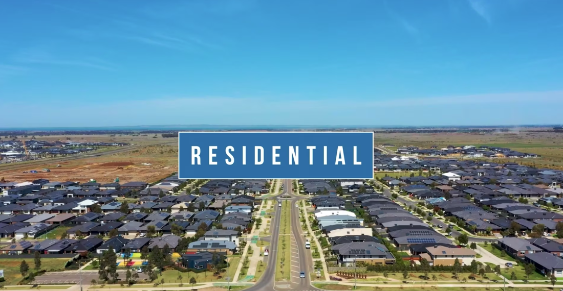 Aerial drone view of modern residential housing estate with central boulevard and surrounding greenfield land under development.