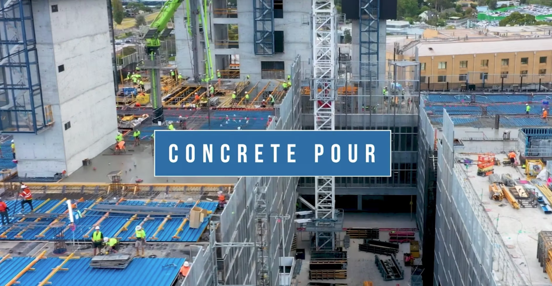 Elevated construction photography showing concrete pour activity, tower crane, formwork and crews across a multi‑storey building site.
