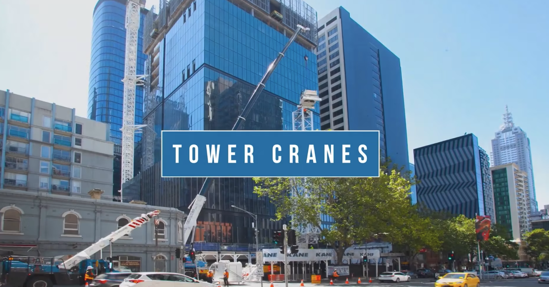 Tower cranes and mobile cranes operating around a glass office high-rise in a busy Melbourne city streetscape.