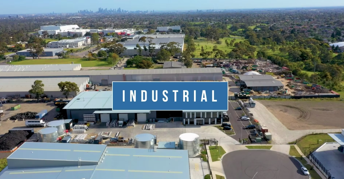 Aerial drone view of industrial warehouses and surrounding urban landscape with bold “Industrial” text overlay.