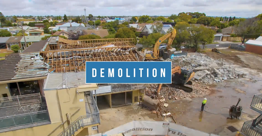 A time-lapse image capturing the demolition of a structure at a construction site, with debris falling and machinery in action.