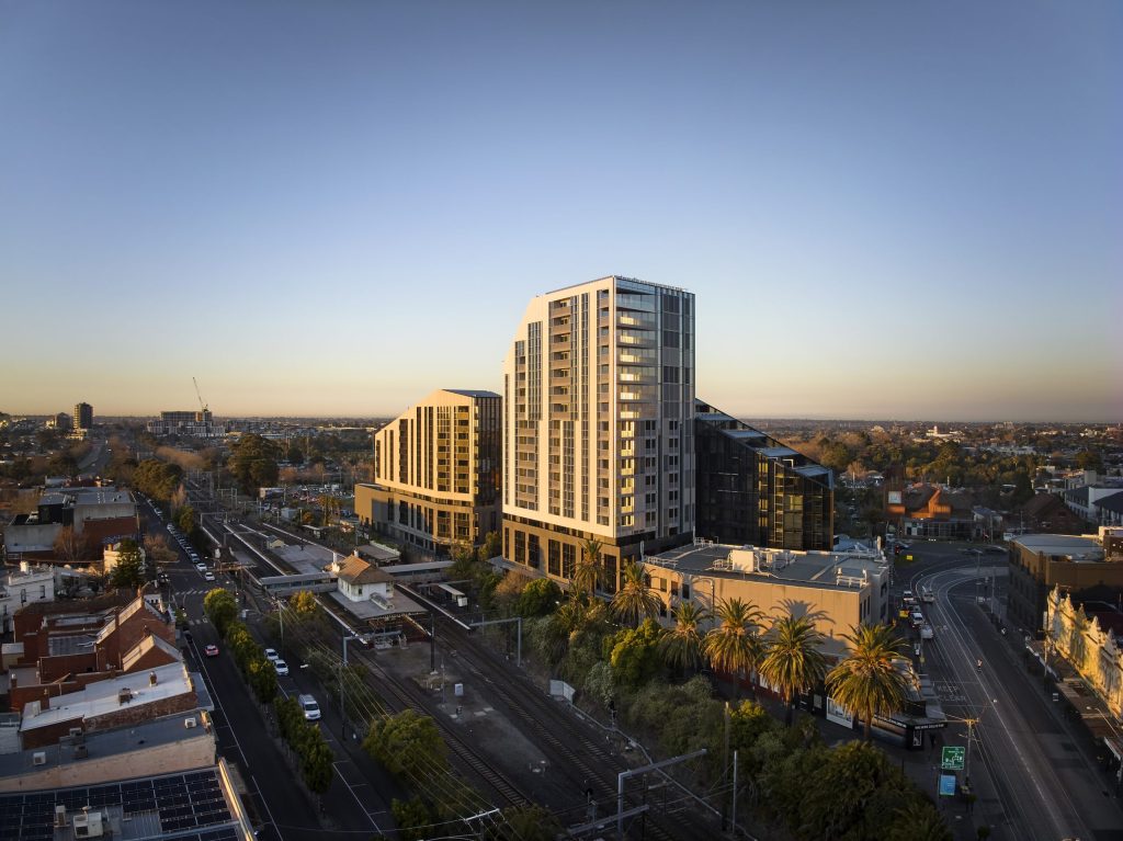 Golden hour aerial view of stepped residential buildings above a rail corridor lined with palm trees.