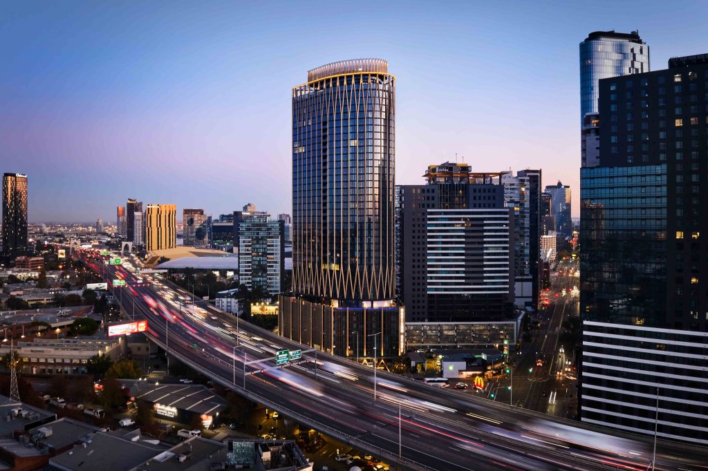 Twilight aerial view of a landmark commercial tower beside a busy freeway with light trails.