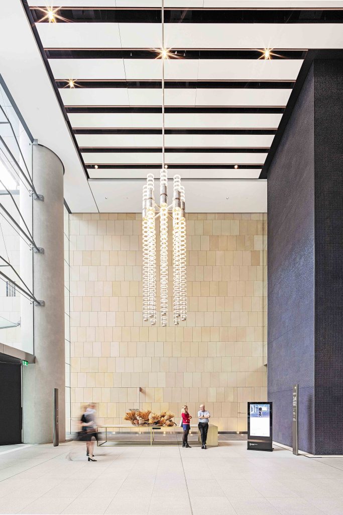 Bright commercial lobby with sculptural chandelier, stone feature wall and people interacting near the reception area.