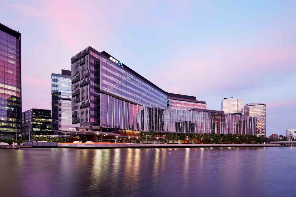 Evening riverfront view of a long glazed commercial building reflecting pink sky across the water.