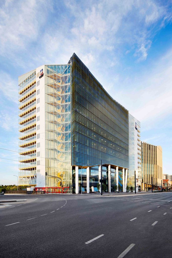 Daytime street view of a glazed office building with curved louvred facade and exposed stair tower.
