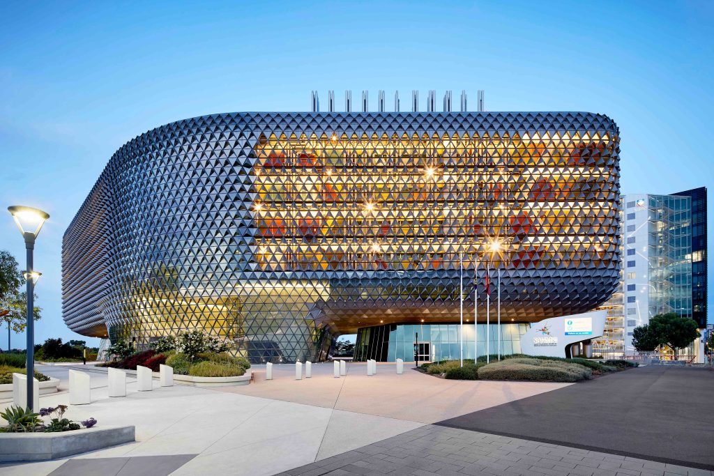 Evening view of a sculptural research building with faceted metal skin and glowing interior levels.