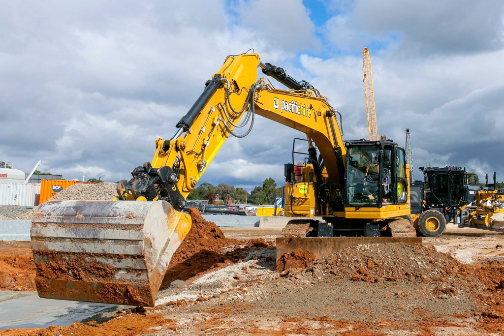 Large yellow excavator digging through soil and gravel on a civil construction site under cloudy skies.