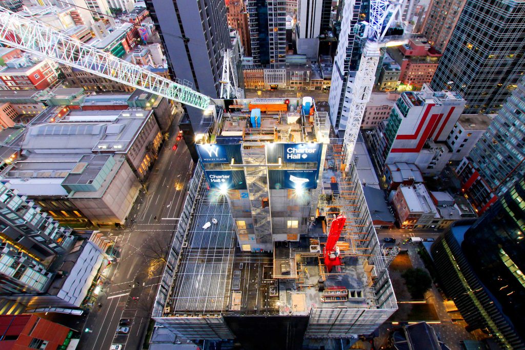 High aerial view of a city tower under construction with cranes and illuminated night-time work areas.