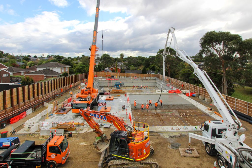 Elevated view of a concrete pour with cranes, pump truck and crews working on a large basement structure.
