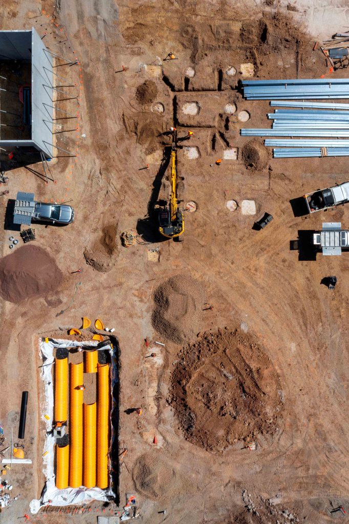 Aerial view of excavator, trenches, drainage tanks and stockpiled material on an active construction site.