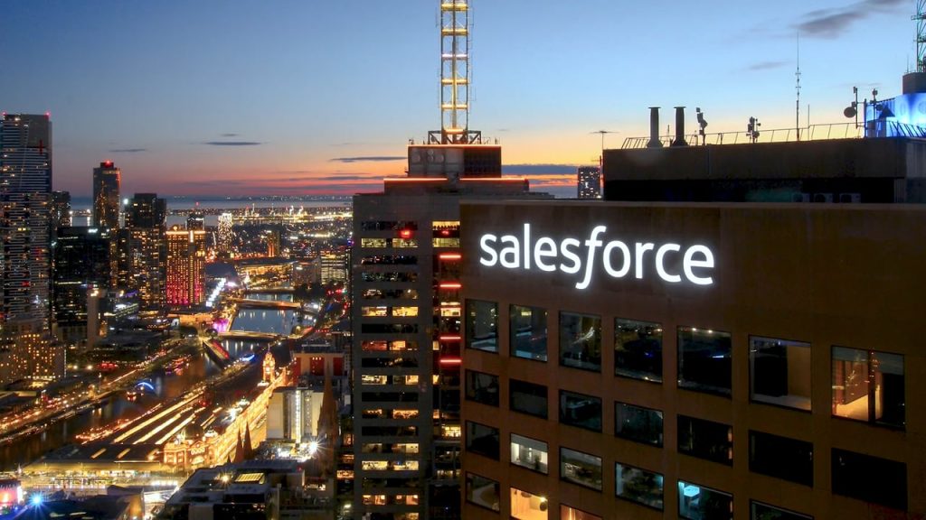 City skyline at dusk with illuminated Salesforce high‑rise overlooking riverfront, bridges and busy inner‑city streets.
